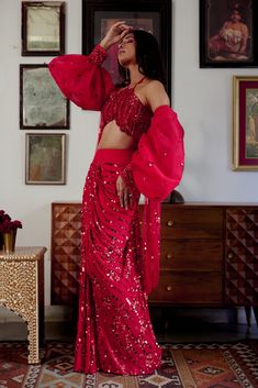 Step into iconic glamour where elegance is draped in the shimmer of scarlet palette for the season’s soirees. Our new-age concept of pre-draped saree features a chic halter neck blouse adorned with nalki crystals embellishment paired up with a sequined pre-draped skirt. Adding a hint of drama the handmade puffer sleeves complete the whole iconic look. • Pre-draped sequined skirt.• Halter-neck blouse adorned with nalki crystals and moti embellishments. • Metal hook at the back side of the blouse to conceal. • Puffed sleeves with an attached sequined dupatta.• Metal zip on the backside of the skirt along with a hook for support.From Moledro’s Fitoor collection. DELIVERY TIMEPlease allow 8-12 weeks for your outfit to arrive. FABRIC DETAILSBlouse: Butterfly Net Skirt: GeorgetteSleeves: Net Pro Red Pre-draped Saree For Party, Red Pre-draped Saree For Evening With Traditional Drape, Draped Sequin Lehenga For Evening, Evening Draped Sequin Lehenga, Pre-draped Party Wear Saree For Gala, Red Georgette Lehenga For Evening, Traditional Drape Saree For Party Wear At Gala, Traditional Drape Saree For Gala Party, Party Wear Saree For Gala With Traditional Drape