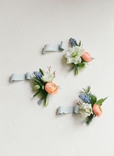 three boutonnieres with flowers and greenery tied to them on a white wall