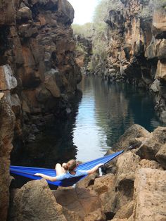 a woman laying in a hammock on top of rocks next to a body of water