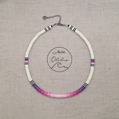 a white and pink beaded bracelet with black beads on a beige background, the necklace has a small circle that says peace on it