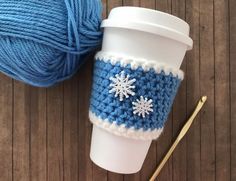 a coffee cup with a crocheted snowflake on it next to a ball of yarn