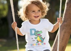 Your kids are going to love this super soft and fun "D is for Dinosaur" tee.  * Our modern unisex fitted shirt style features a crewneck and contoured side seams for a stylish trendy t-shirt. * All our tees and body suits come with a tear-away label for a scratch-free wearing experience * White shirts and bodysuits are 100% ringspun cotton. Heather color (grey) is  52% cotton, 48% polyester. Please make sure you check our size cards before you place your order.   If you have any questions please let us know. We hope to earn your business.  Thank You Fun Short Sleeve T-shirt With Dinosaur Print, Playful Unisex T-shirt With Character Print, Cute Letter Print T-shirt For Playtime, Funny Short Sleeve T-shirt For Playtime, Playful Tops With Funny Print For Playtime, Playful Graphic Print T-shirt For Daycare, Funny Character Print Tops For Playtime, Playful Crew Neck Top With Name Print, Playful Letter Print Tops For Playtime