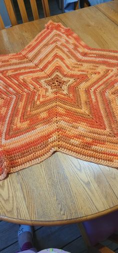 a wooden table topped with an orange and white afghan on top of a wooden floor