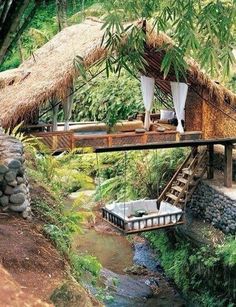 a house in the middle of some trees with a bridge over it and a bed on top