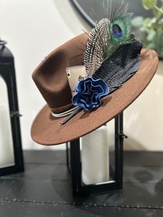 A hip western style hat that that fits both formal and casual styles. The hat band, black feathwr and blue flower are designed using premium leather. This is one size fits all with an inner lace inside the crown allowing you to adjust the size. Brown Top Hat For Kentucky Derby And Country Events, Elegant Brown Fedora For Country Events, Brown Western Fedora For Party, Western Style Brown Fedora For Party, Western Brown Mini Fedora Hat, Brown Hat Bands For Fall Party, Brown Hat Bands For Party In Fall, Brown Fedora Hat With Feathers, Western-themed Fedora With Feather Trim