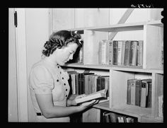 an old photo of a woman reading a book in front of some bookshelves