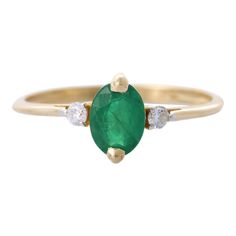 an emerald and diamond ring with two diamonds on the side, set in yellow gold