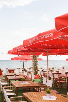 tables and chairs with red umbrellas over them at an outdoor restaurant on the beach