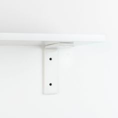 a white shelf with two black dots on the bottom and one in the middle, against a white wall