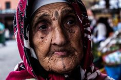 an old woman with wrinkles on her face and scarf around her head, looking at the camera