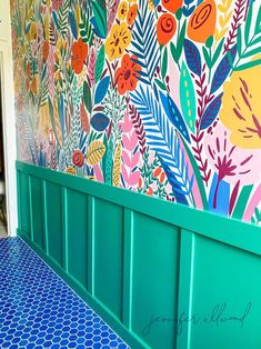 a bench sitting in front of a colorful wall with flowers on it's side