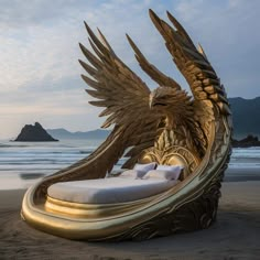 a large golden bird sculpture sitting on top of a sandy beach next to the ocean