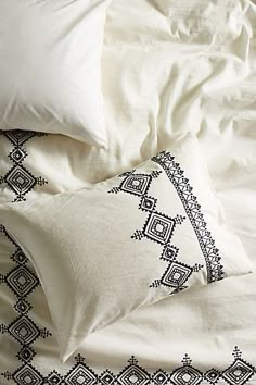 an unmade bed with white sheets and black embroidered pillow cases on top of it