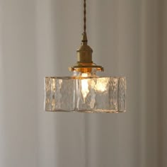 a clear glass light fixture hanging from a metal ceiling hook in a white walled room