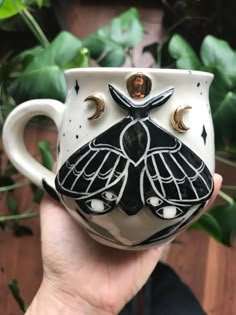 a hand holding a white and black coffee cup with a butterfly on it's face