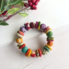 a bracelet made out of different colored beads next to a potted plant with red berries