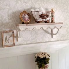 a shelf with flowers and pictures on it in a room that has white wallpaper