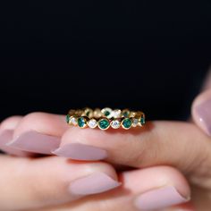 a woman's hand holding a gold ring with emeralds and diamonds on it