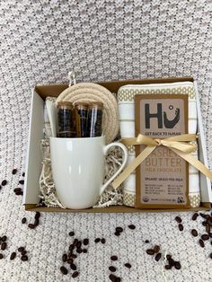 a coffee cup and two mugs in a gift box on top of a bed