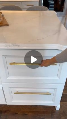 a person is opening the drawer on a white kitchen countertop with gold handles and pulls