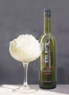 a bottle of olive oil next to a wine glass filled with ice cream on a table