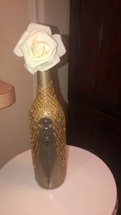 a gold vase with a white rose in it on top of a small round table