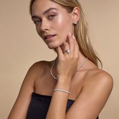 a woman in a black dress is posing with her hand on her face and wearing two diamond bracelets