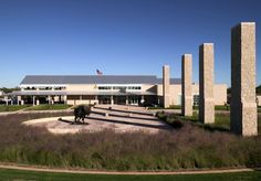 an animal statue in front of a building with columns and grass around it on a sunny day