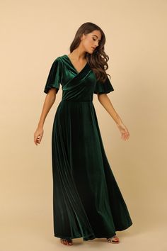 a woman wearing a green velvet dress with short sleeves and an open back, standing in front of a beige background