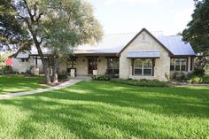 a house that is in the middle of some grass with trees and bushes around it