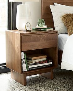 a nightstand with books and a clock on it next to a bed in a bedroom