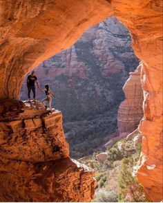 two people are standing on the edge of a cliff and looking out into the canyon