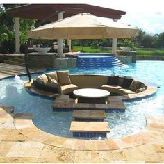 an outdoor living area with couches, umbrellas and water feature in the pool