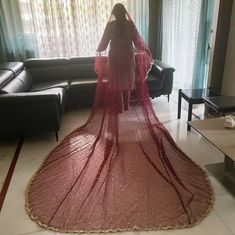 a woman in a red dress is standing near a couch with a long veil on it