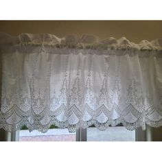 a window with white curtains and lace on the valance, in front of a brick wall