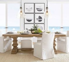 a dining room table with white chairs and pictures on the wall in front of it