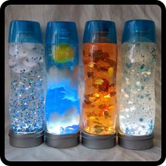 four different colored glass vases sitting on top of a white sheet