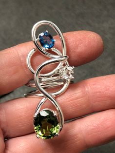 I've created this Bohemian abstract large finger ring, a true statement piece, in sterling silver, which features a 10x8mm oval Peridot, a 6mm White Topaz and an 8x6mm Blue Zircon. I make everything in 925 Sterling Silver and can Rhodium plate if you wish over the piece. I use AA+ grade gemstones in my work. The ring base is 12 gauge round sterling silver wire. No two are alike has I hand-fabricate one-of-a-kind designs. This statement ring is sturdy and I soldered many contact points and harden Unique Sterling Silver Ring With Gemstone Accents, Sterling Silver Rings With Gemstone Accents, Unique Sterling Silver Rings With Gemstone Accents, Unique Sapphire Rings With Gemstone Accents, Fusion Style Multi-stone Open Ring Jewelry, Unique Blue Topaz Birthstone Jewelry, Unique Multi-stone Sapphire Jewelry, Topaz Jewelry With Gemstone Accents, Unique Multi-stone Blue Topaz Ring