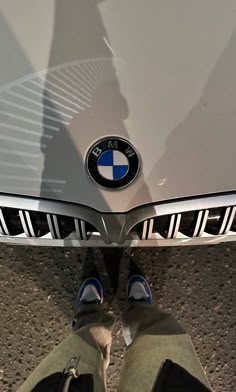 the front end of a bmw car with its emblem on it's grill and two people standing next to it