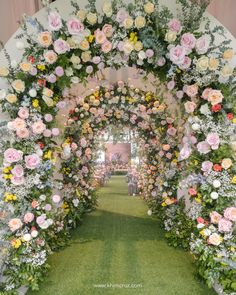 an archway decorated with pink, yellow and white flowers in the middle of a grass field