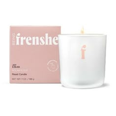 a white candle sitting next to a pink box on a white surface with the letter f in it