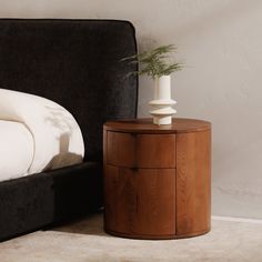 a white vase with a plant on top of it next to a black couch and bed