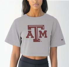 Elevate your Aggie game day attire with our Women's Texas A&M Logo Crop Top, a timeless piece that exudes pride and tradition. Crafted from premium 100% cotton, this tee ensures superior comfort during those intense moments cheering on the Aggies at Reed Arena or exploring the scenic beauty of Aggieland. Featuring the iconic Texas A&M logo front and center, this crop top is a true testament to your Aggie spirit. Whether you're attending class or hitting up Northgate for post-game celebrations, t Varsity Cotton Top With Team Logo, Varsity Cotton Tops With University Logo, Cotton Varsity Top With University Logo, Collegiate Tops With University Logo For Game Day, Collegiate Athletic Heather Tops For Game Day, Collegiate Style Tops In Athletic Heather For Game Day, Sporty University Logo Tops For Sports, Sporty Tops With University Logo For Sports, Sporty University Logo Sports Tops