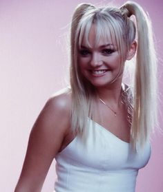 a woman with long blonde hair wearing a white dress and smiling at the camera while standing in front of a pink background