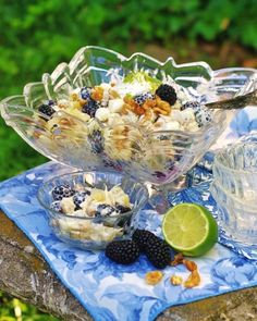 a glass bowl filled with fruit sitting on top of a blue table cloth next to two glasses