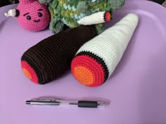 two crocheted toys sitting on top of a purple table next to a pen