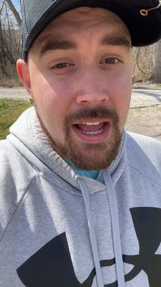 a man wearing a black hat and gray hoodie is posing for the camera with his mouth open