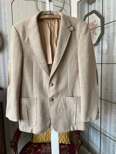 "This jacket is made from wool in timeless beige, in a fine herringbone pattern. It has the original turtle buttons in the front and on the cuffs, two front pockets and two inside pockets, and it's partially lined with tan silky lining. The label reads \"Tailored Especially for The Men's Shop Claremore Okla.\" The measurements, taken with the jacket lying flat, are: shoulder to shoulder, 18 inches; armpit to armpit, 20 inches; sleeves, 25 inches; length, 31 1/2 inches; bottom edge, 25 inches. In very good condition." Beige Long Sleeve Tweed Jacket For Semi-formal Occasions, Beige Tweed Jacket With Notch Lapel And Pockets, Beige Sport Coat With Welt Pockets And Suit Collar, Beige Tweed Jacket With Lapel Collar For Semi-formal Occasions, Tailored Beige Tweed Jacket With Lapel Collar, Beige Single Breasted Tweed Jacket With Notch Lapel, Tailored Beige Tweed Jacket With Suit Collar, Beige Single-breasted Tweed Jacket With Notch Lapel, Cream Single Breasted Blazer With Suit Collar