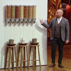 a man standing next to two wooden stools in front of a wall with spices on it