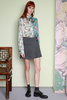 a woman standing in front of a wall wearing a shirt and skirt with flowers on it